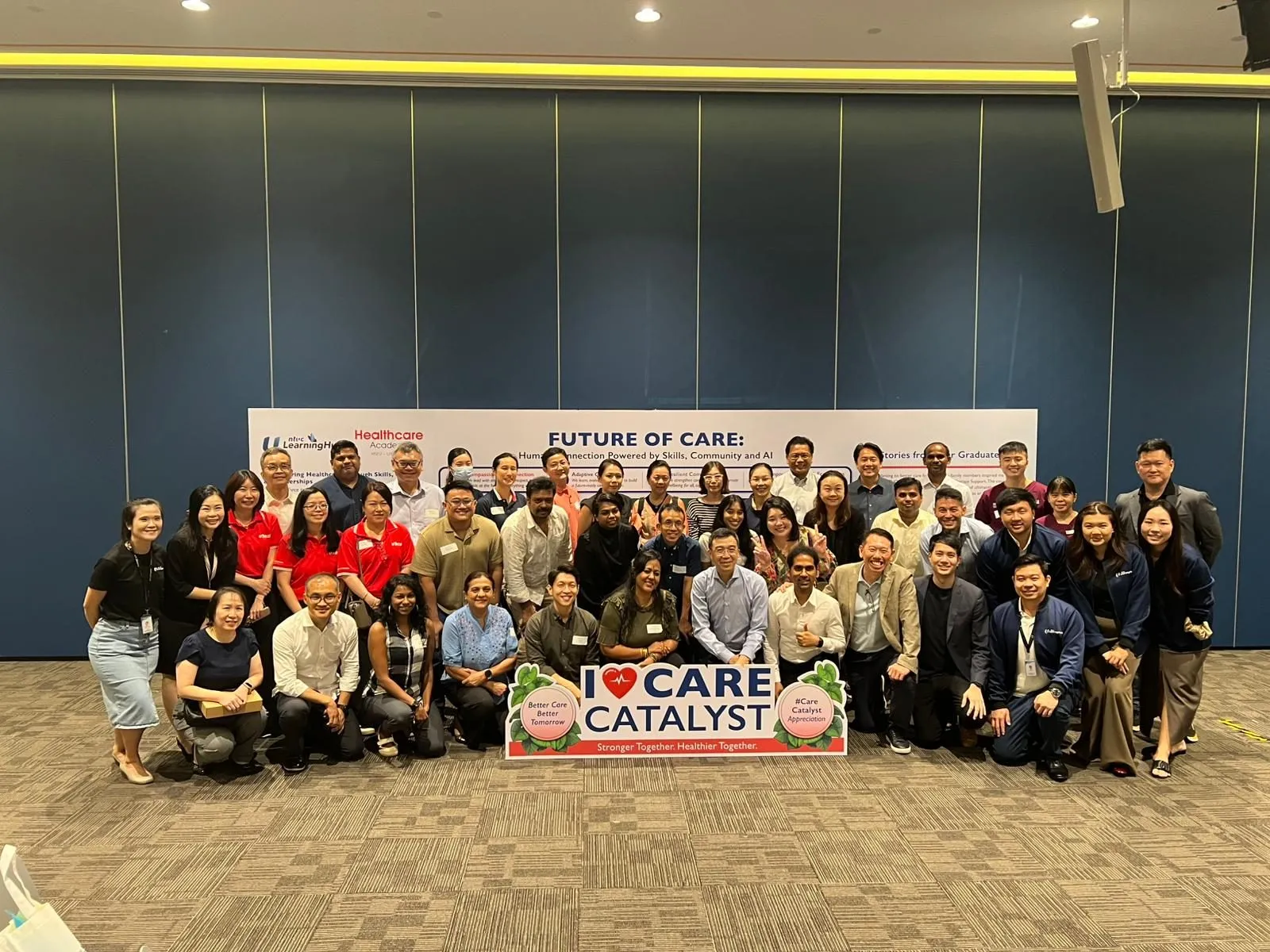 Group photo of FT Academy and NTUC LearningHub Healthcare Sector event attendees, holding a Care Catalyst sign in front of the Future of Care banner