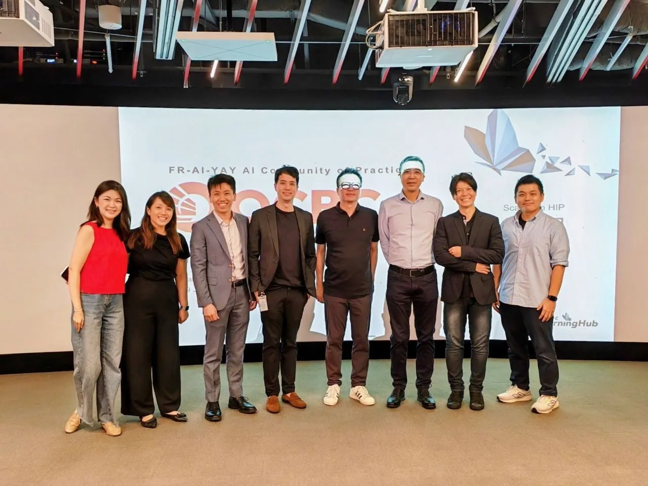 The FT Academy and NTUC LearningHub team standing together in front of the FR-AI-YAY AI Community of Practice screen.
