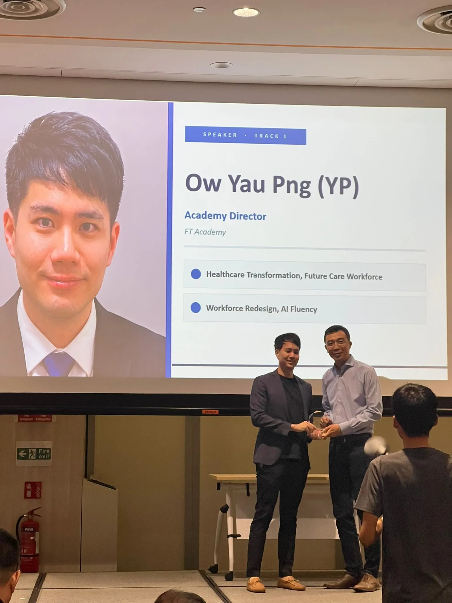 Yau Png Ow receiving a token of appreciation on stage, with his speaker profile displayed on screen identifying him as Academy Director of FT Academy
